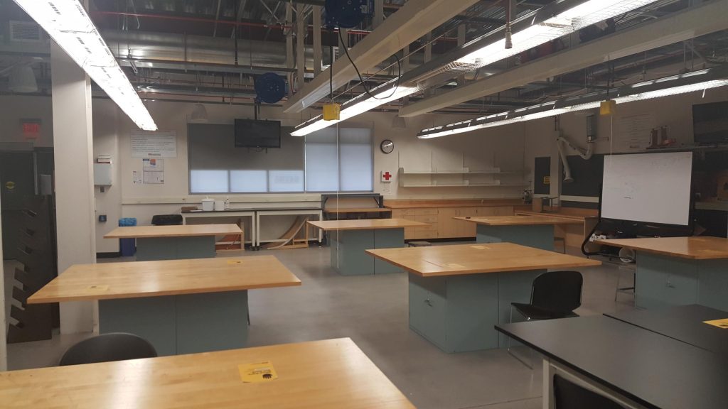 A classroom with several Highland tables, a couple of chairs and a whiteboard.