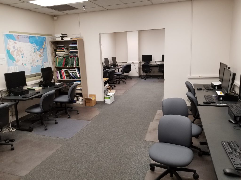 Instructional lab with two rooms and several desks, computers, printers, and chairs along the walls.